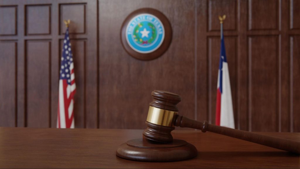 Wooden gavel in a courtroom with Texas and U.S. flags in the background, symbolizing legal proceedings.