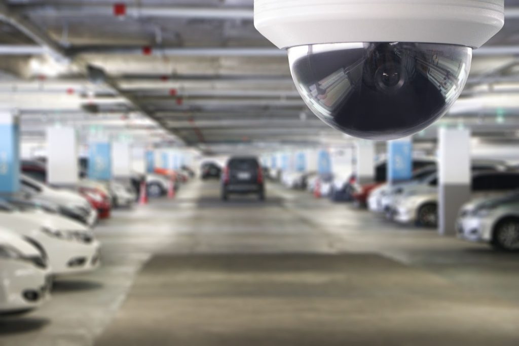Security camera in focus at the forefront, overseeing a blurred underground parking lot, symbolizing measures to prevent car theft.