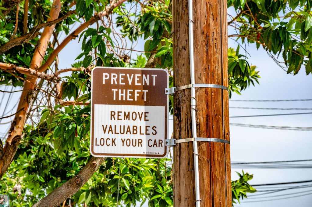 Sign attached to a pole reading 'PREVENT THEFT REMOVE VALUABLES LOCK YOUR CAR,'.