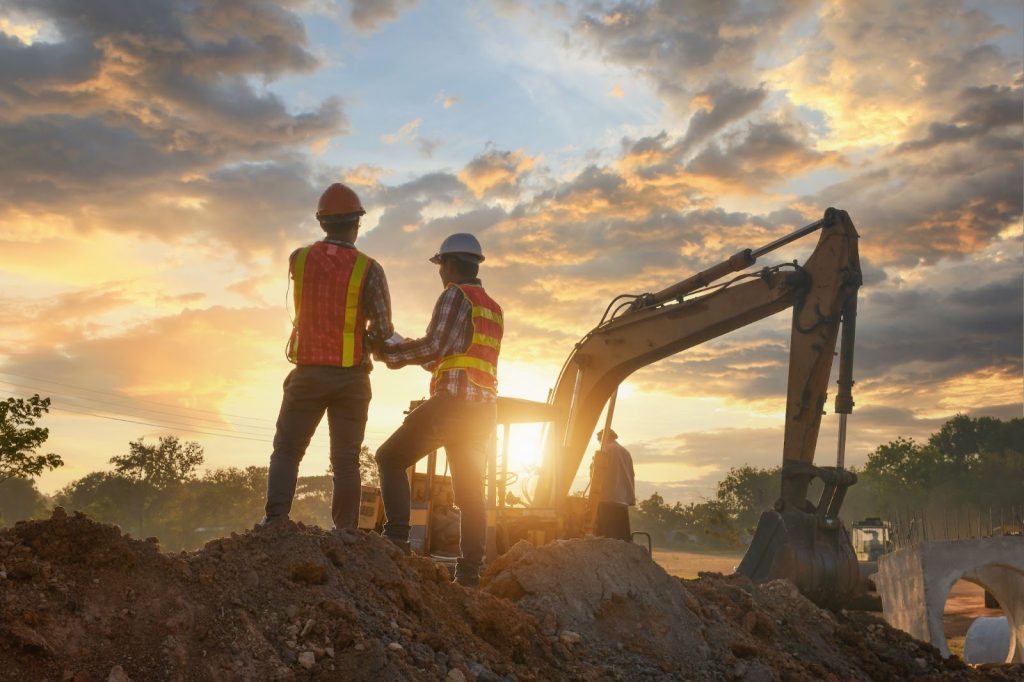 Des ouvriers de la construction et une pelleteuse sur un chantier serein au coucher du soleil.