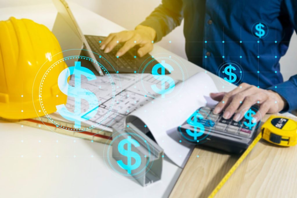 Personne travaillant sur un ordinateur portable et examinant des plans architecturaux avec des signes numériques en dollars.