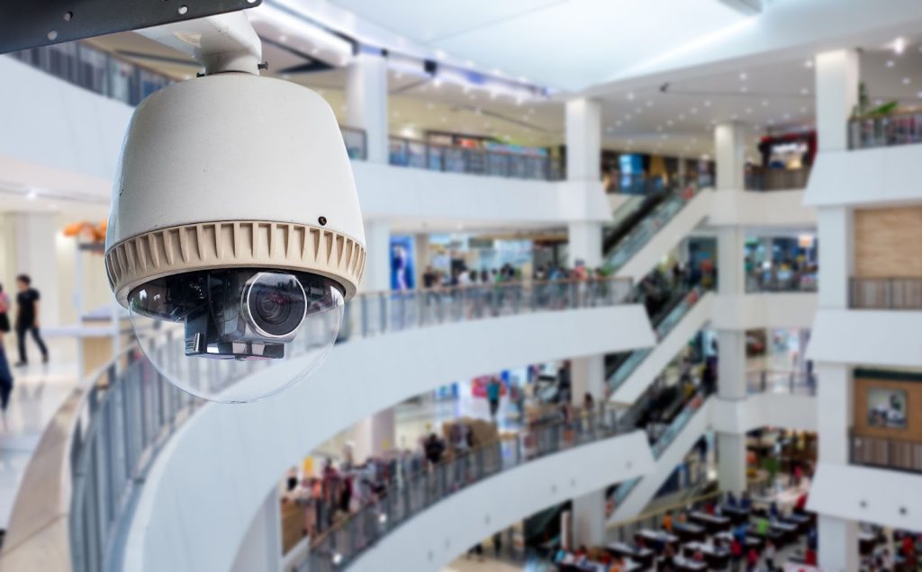 Dome security camera overlooking a busy shopping mall interior.