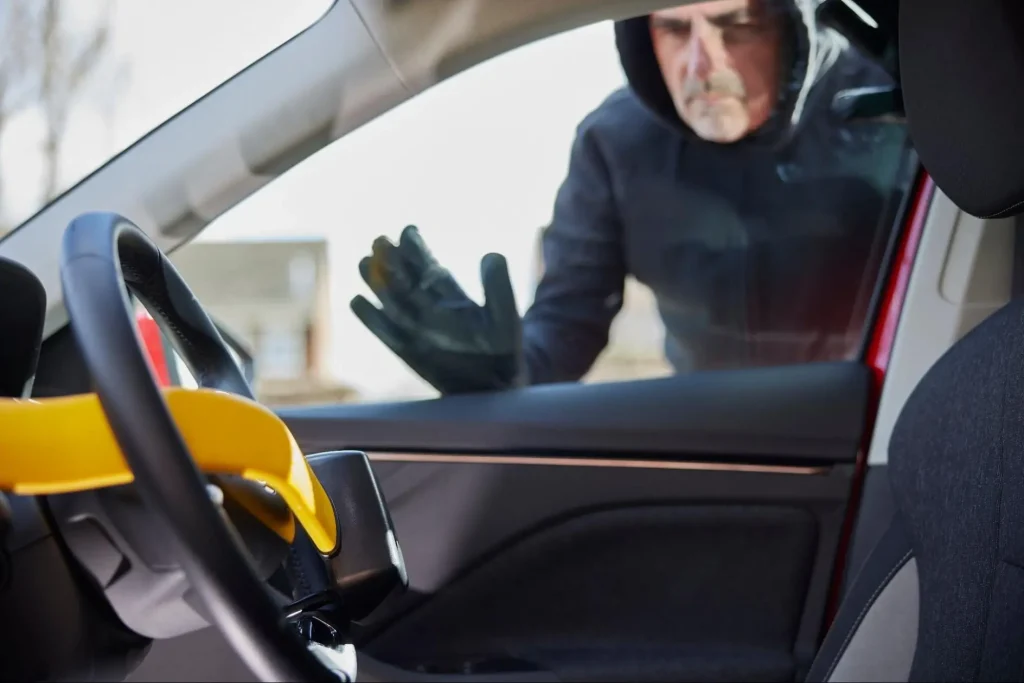 Thief wearing gloves attempting to steal a car with a yellow steering wheel lock in place.