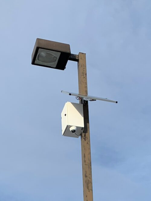 Security camera attached to a high pole overlooking an area.