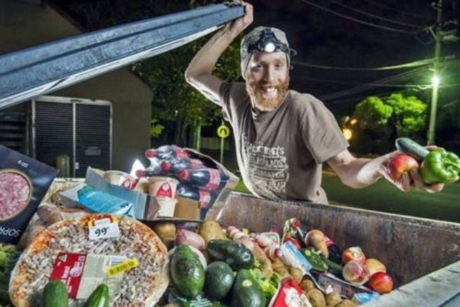 Homme souriant présentant des aliments récupérés dans une benne à ordures la nuit.