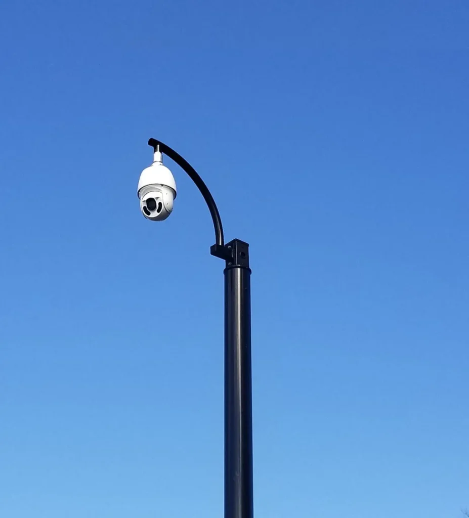 Caméra PTZ extérieure montée sur un grand poteau, surveillant un espace ouvert.