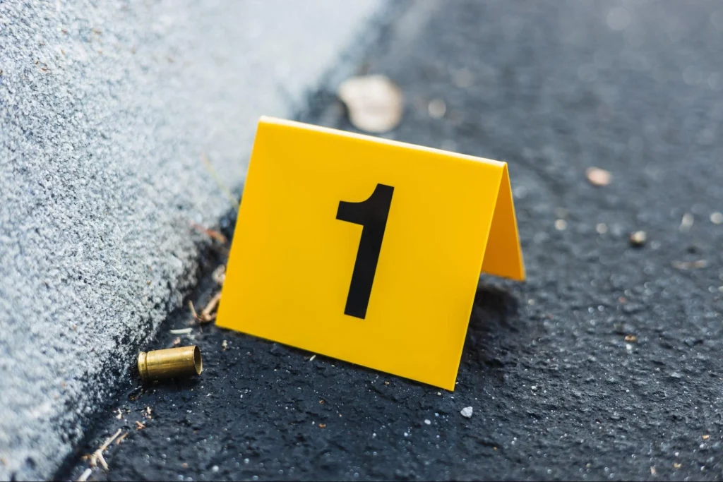 Yellow evidence marker number one placed next to a bullet casing on asphalt at a crime scene in Long Beach.