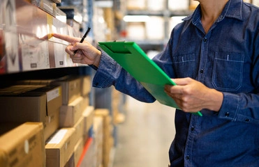 Employee conducting manual inventory count using clipboard in warehouse aisle